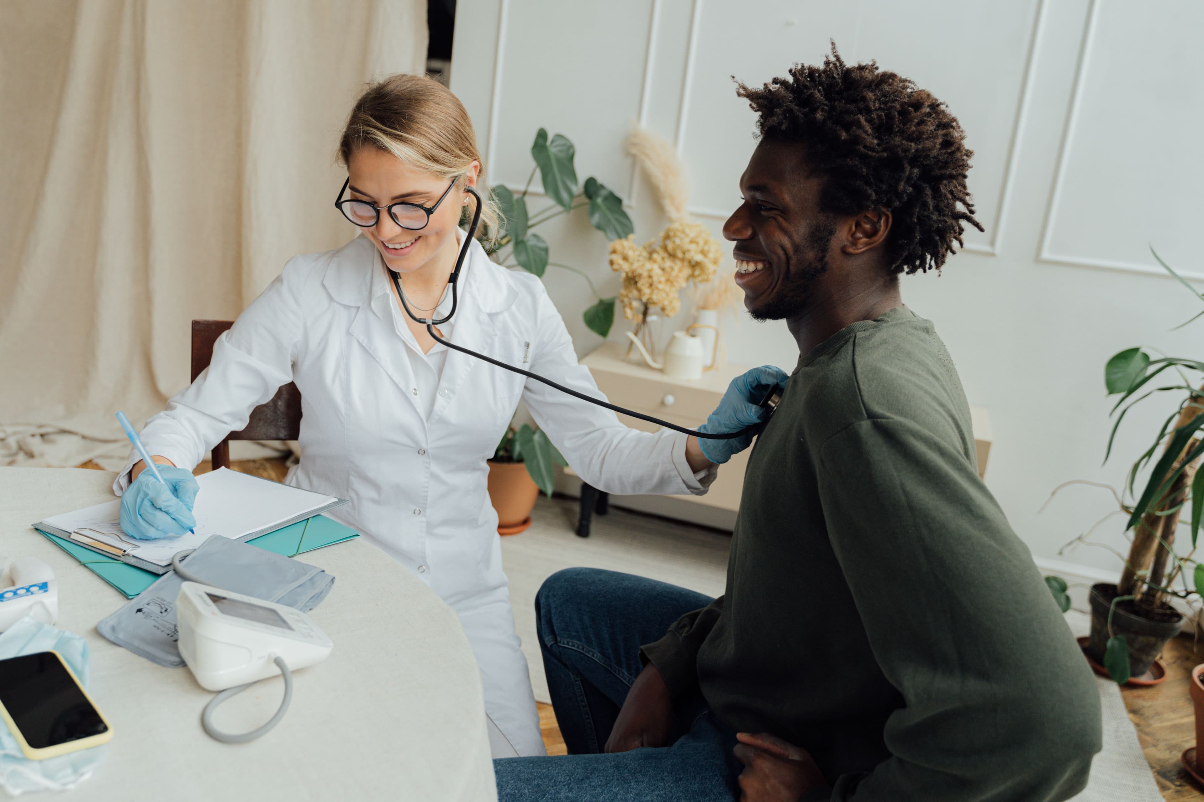 A doctor listens to a smiling patient's chest with a stethoscope during an in-clinic consultation